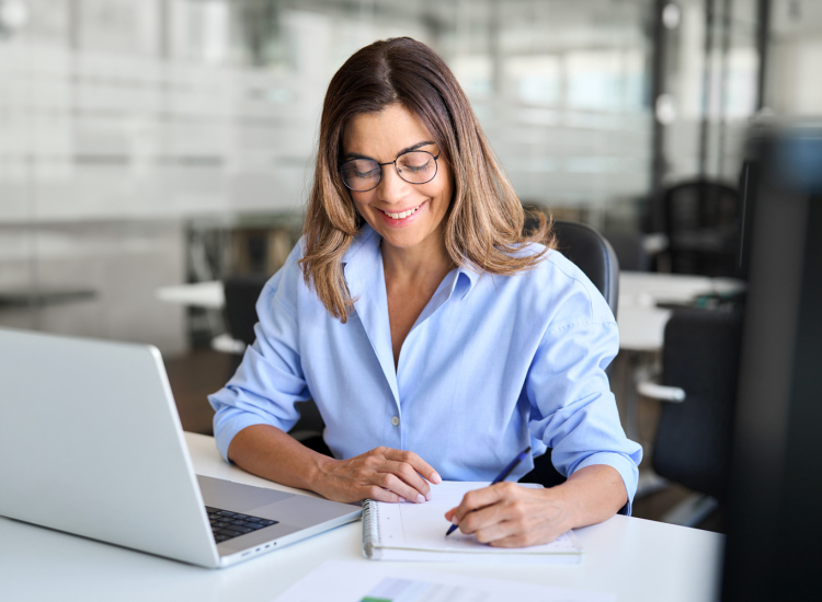 Vrouw volgt een training, zit aan haar bureau met laptop en maakt aantekeningen