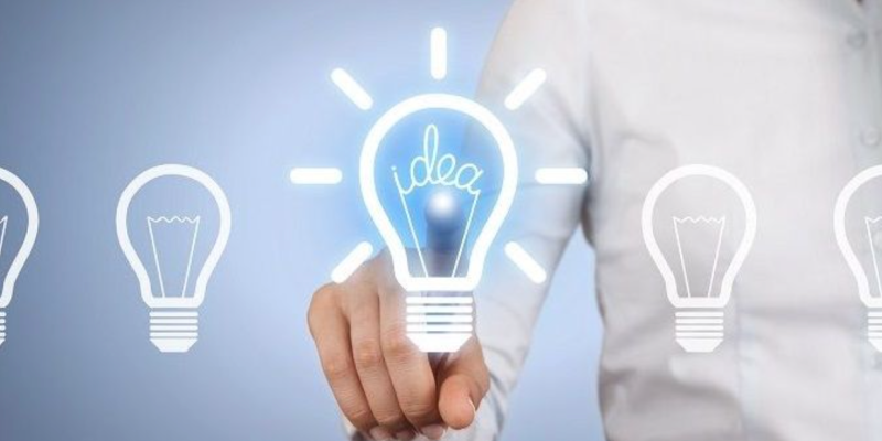 Persoon in wit overhemd wijst naar verlichte gloeilamp met 'idea', omringd door vier niet-verlichte lampen op blauwe achtergrond.